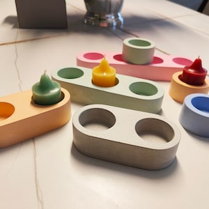 May include: Set of six tealight candle holders in various colours, including light blue, light green, light pink, and grey. Each holder has a smooth, textured surface and is designed to hold a small candle.