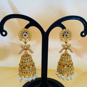 May include: Gold tone dangle earrings with white and green stones, a red stone, and a pearl drop.