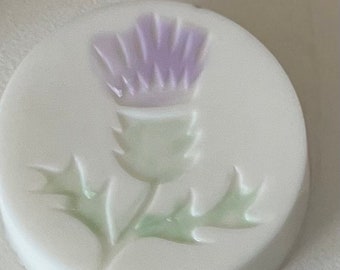 May include: A white ceramic button with a raised design of a purple thistle flower.