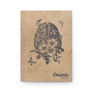 May include: A brown notebook with a black and white illustration of a brain with flowers and butterflies. The text "Amanda BSN, RN" is printed on the cover.