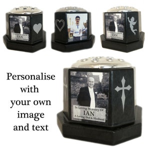 Puede incluir: Jarrón hexagonal negro con tapa plateada y un marco de fotos. El marco de fotos tiene una foto en blanco y negro de un hombre y el texto "In Loving Memory Of IAN A Loving Dad & Husband".