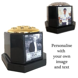 Puede incluir: Jarrón de flores hexagonal negro con parte superior dorada y un inserto para fotos. El inserto para fotos muestra a un hombre con traje y corbata. El texto en el jarrón dice "In Loving Memory Of IAN A Loving Dad & Husband".