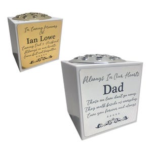 May include: Two white memorial vases with silver tops. One has a gold plaque with the text "In Loving Memory Of Ian Lowe". The other has a silver plaque with the text "Always In Our Hearts Dad".