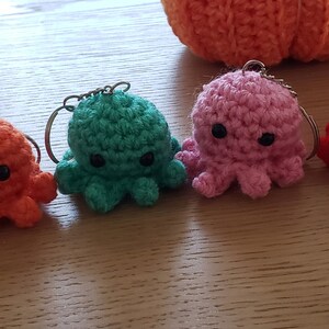 May include: Seven crocheted octopus keychains in different colors, including purple, orange, green, pink, red, and blue with a multi-colored octopus. Each octopus has a small black button eyes.