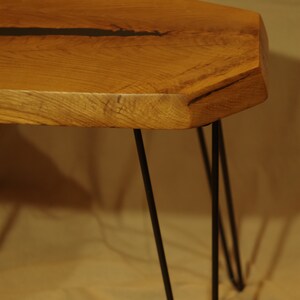 Op de afbeelding: Een houten tafel met een live edge blad en zwarte metalen haarspeldpoten. Het tafelblad heeft een natuurlijke houtnerf en een donkerbruine harsvulling.