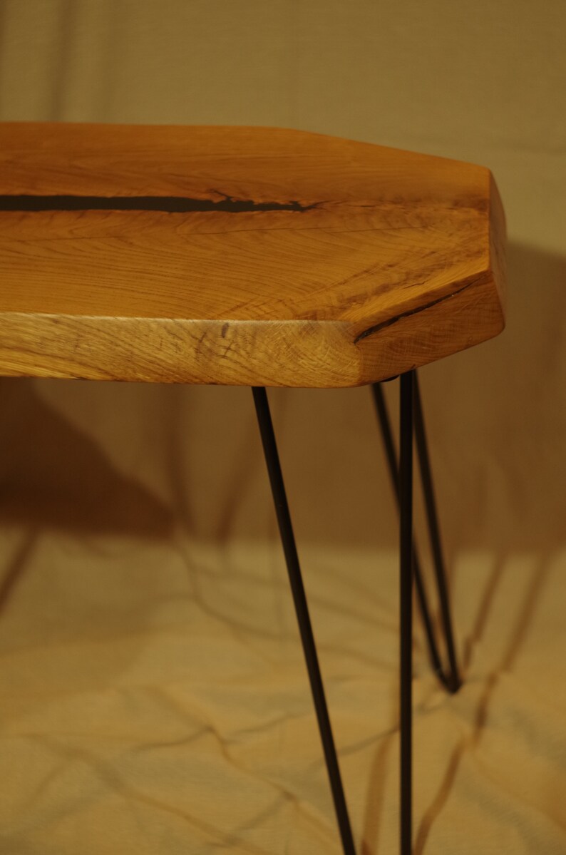 Op de afbeelding: Een houten tafel met een live edge blad en zwarte metalen haarspeldpoten. Het tafelblad heeft een natuurlijke houtnerf en een donkerbruine harsvulling.