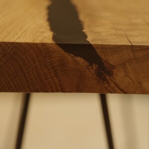 Op de afbeelding: Een houten tafelblad met een zwarte harsinleg. De tafel heeft zwarte metalen haarspeldpoten.