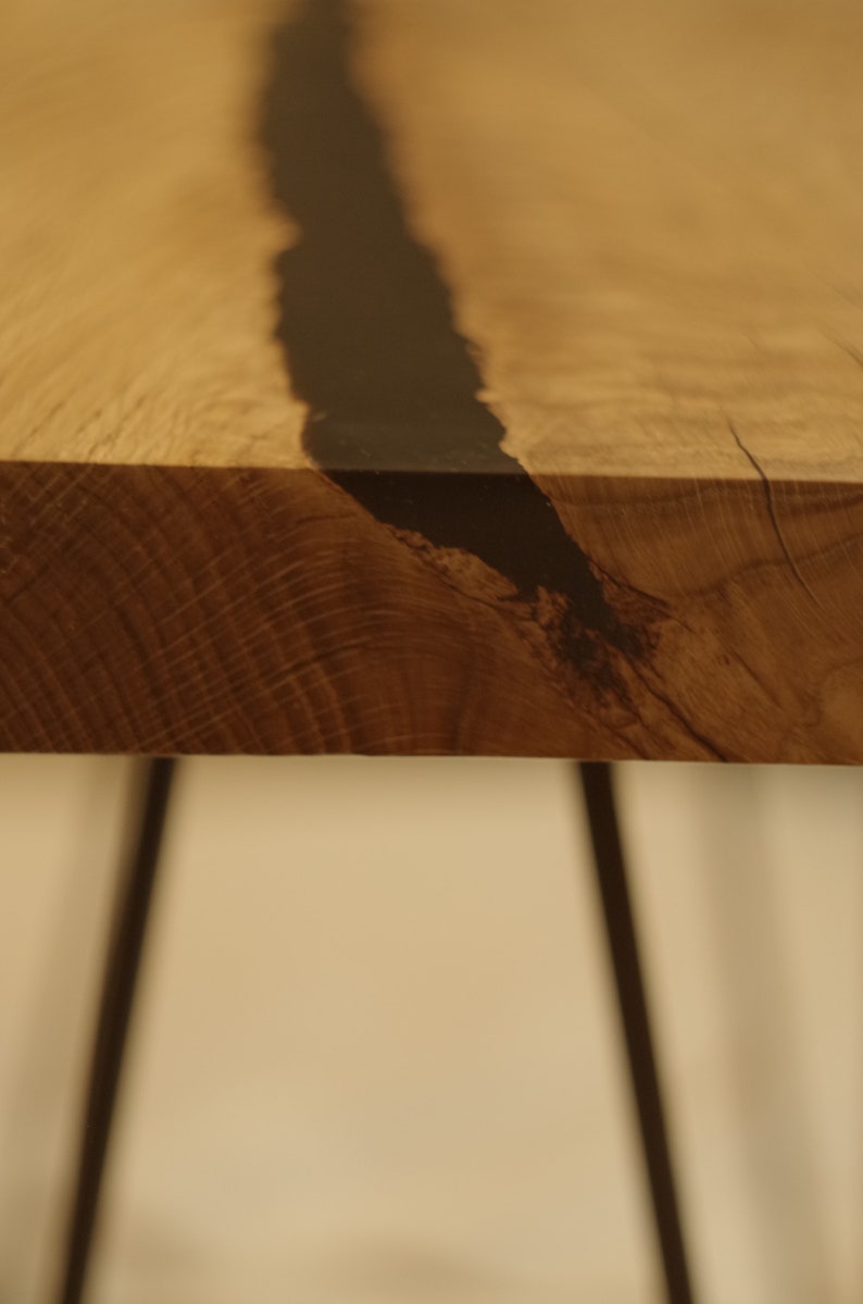 Op de afbeelding: Een houten tafelblad met een zwarte harsinleg. De tafel heeft zwarte metalen haarspeldpoten.