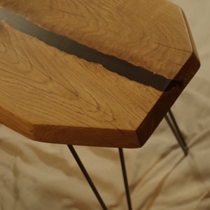 Op de afbeelding: Een zeshoekige houten tafel met een zwarte harsinleg en haarspeldpoten. De tafel is gemaakt van natuurlijk hout met een rustieke afwerking.