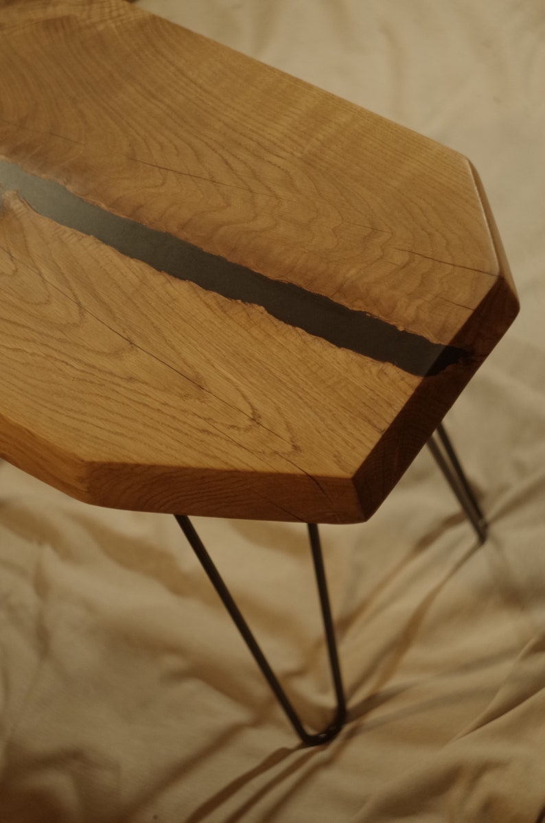 Op de afbeelding: Een zeshoekige houten tafel met een zwarte harsinleg en haarspeldpoten. De tafel is gemaakt van natuurlijk hout met een rustieke afwerking.