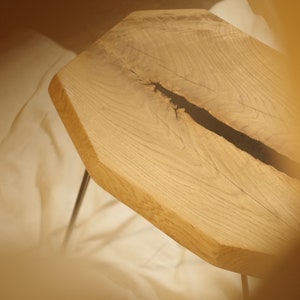 Op de afbeelding: Een houten tafelblad met een natuurlijke rand en een zwarte harsvulling in een scheur. Het tafelblad wordt ondersteund door twee zwarte haarspeldpoten.