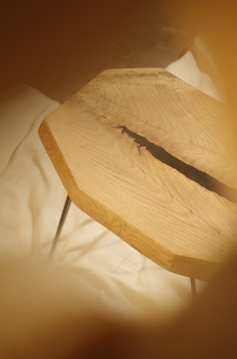 Op de afbeelding: Een houten tafelblad met een natuurlijke rand en een zwarte harsvulling in een scheur. Het tafelblad wordt ondersteund door twee zwarte haarspeldpoten.
