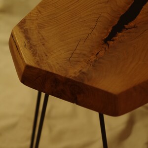 Op de afbeelding: Een houten tafel met een natuurlijke houtkleur en een zwarte harsinleg. De tafel heeft een unieke, onregelmatige vorm en wordt ondersteund door vier zwarte haarspeldpoten.