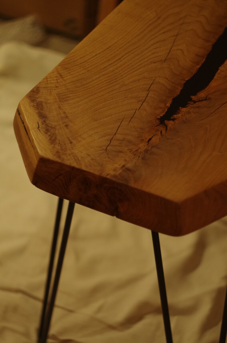 Op de afbeelding: Een houten tafel met een natuurlijke houtkleur en een zwarte harsinleg. De tafel heeft een unieke, onregelmatige vorm en wordt ondersteund door vier zwarte haarspeldpoten.