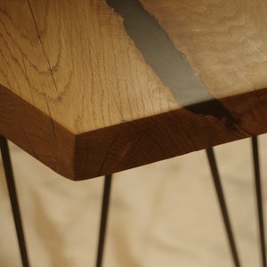 Op de afbeelding: Een houten tafelblad met een zwarte harsinleg. De tafel heeft een natuurlijke houtkleur en wordt ondersteund door dunne zwarte metalen poten.