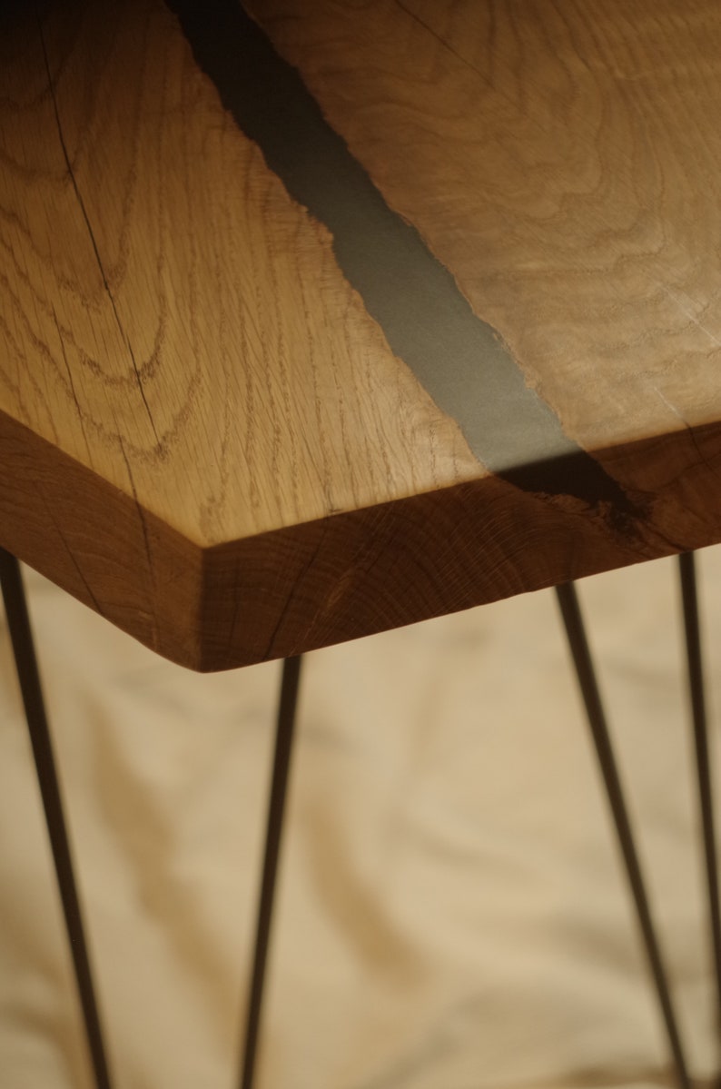 Op de afbeelding: Een houten tafelblad met een zwarte harsinleg. De tafel heeft een natuurlijke houtkleur en wordt ondersteund door dunne zwarte metalen poten.