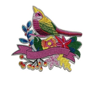 May include: Embroidered patch featuring a colorful bird perched above a floral arrangement and a blank pink banner. The bird has yellow, pink, green, and red feathers. The flowers include red, yellow, and pink blooms, with green leaves and blue berries.
