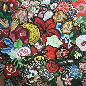 May include: A collection of colorful embroidered patches featuring various floral designs. The patches include roses, leaves, and other botanical elements in shades of red, pink, yellow, and blue. Some patches have text.