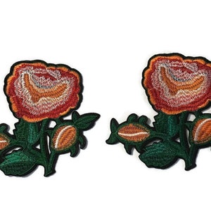 May include: Two embroidered floral patches. Each patch features a large, open rose in shades of red, orange, and yellow, with detailed stitching. Green leaves and buds accompany the rose, all outlined in black.