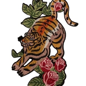 May include: An embroidered patch featuring a tiger in a stretching pose with orange and black stripes. The tiger is surrounded by red roses with green leaves and stems. The design is detailed with visible thread textures and a black border outline.