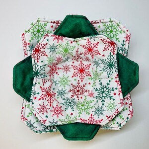 May include: A set of three green and white fabric bowl cozies with a snowflake pattern. The cozies are made of a soft, quilted fabric and are designed to protect bowls from heat.