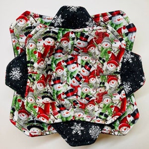 May include: Set of three quilted fabric bowl cozies featuring a snowman pattern in red, green, and white on a white background. The cozies are lined with black fabric with white snowflakes.
