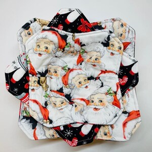 May include: Set of four black and white fabric pot holders with a Christmas theme. The pot holders feature a repeating pattern of Santa Claus faces with red hats and white beards. The pot holders have a black and white snowflake pattern on the back.