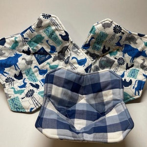May include: Three fabric bowl cozies. Two are patterned with blue farm animals, windmills, and text on a white background. The third is blue and white plaid. These cozies are designed to keep bowls warm.