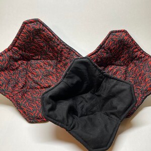 May include: Three quilted bowl cozies in different sizes. The cozies are black on the inside and have a red and black chili pepper print on the outside.