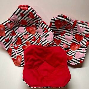 May include: Three fabric bowls with a black and white striped pattern and pink and red hearts. The bowls are lined with red fabric.