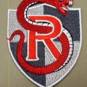 May include: A red snake with a white outline wraps around a red letter "R" on a grey and white chequered shield. The snake has a red head with a white outline and a white fang.