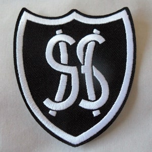 May include: A black and white shield-shaped patch with a white border. The patch features the intertwined letters "S" and "f" in white, centered on a black background. The patch is likely an emblem or logo.