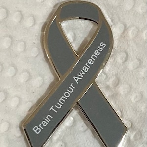May include: Gray ribbon pin with the words "Brain Tumour Awareness" printed in white.