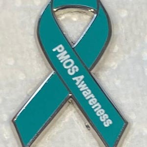 May include: A teal awareness ribbon pin with a silver metal border. The text PMOS Awareness is printed in white capital letters along the right side of the ribbon loop. The design features a classic looped shape with two angled ends at the bottom.
