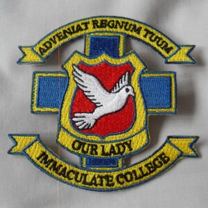 Puede incluir: Parche bordado amarillo y azul con una paloma blanca sobre un escudo rojo, rodeado de una pancarta amarilla con el texto "Our Lady Immaculate College" y una pancarta más pequeña con el texto "Adveniat Regnum Tuum".