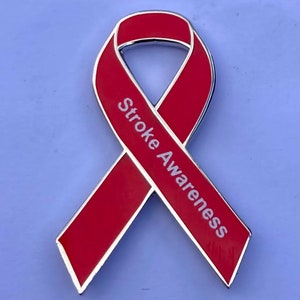 Op de afbeelding: Rode lint-speld met zilveren rand en de tekst "Stroke Awareness" in wit.