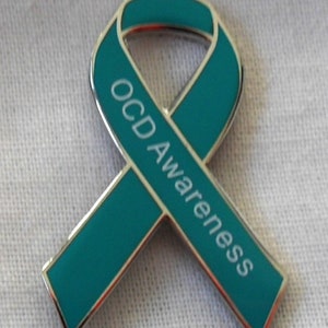 May include: Teal blue ribbon pin with the words "OCD Awareness" printed in white.