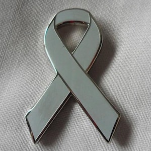 May include: A silver ribbon pin with a polished finish. The ribbon is a classic looped design, with a silver border. The pin is likely made of metal and is set against a neutral background.