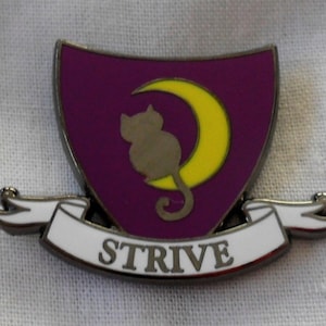 May include: A purple and yellow enamel pin featuring a crescent moon with a cat sitting on it. The pin has a white banner with the word "STRIVE" on it.