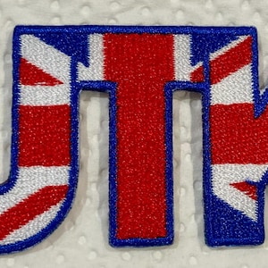 May include: Embroidered patch displaying the letters UTK, each incorporating the Union Jack flag in red, white, and blue. The letters are outlined in blue and stitched onto a white fabric. Suitable for customising clothing or accessories.