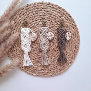 Könnte beinhalten: Drei Makramee-Schlüsselanhänger mit Holzetiketten. Die Etiketten sind mit den Namen "Marie", "Oma" und "Julia" graviert. Die Schlüsselanhänger sind in Beige, Weiß und Braun.