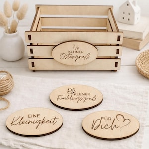 Puede incluir: Una caja de madera con tres placas ovaladas de madera. La caja tiene el texto "Kleiner Ostergruß" en una placa ovalada. Las otras placas tienen el texto "Eine Kleinigkeit", "Für Dich" y "Kleiner Frühlingsgruß".