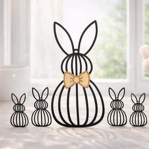 Könnte beinhalten: Ein schwarzes Osterhasen-Familien-Set aus Metall. Der große Hase hat eine Holzfliege. Das Set enthält einen großen Hasen und vier kleinere Hasen. Die Hasen sind auf einer weißen Oberfläche aufgereiht.