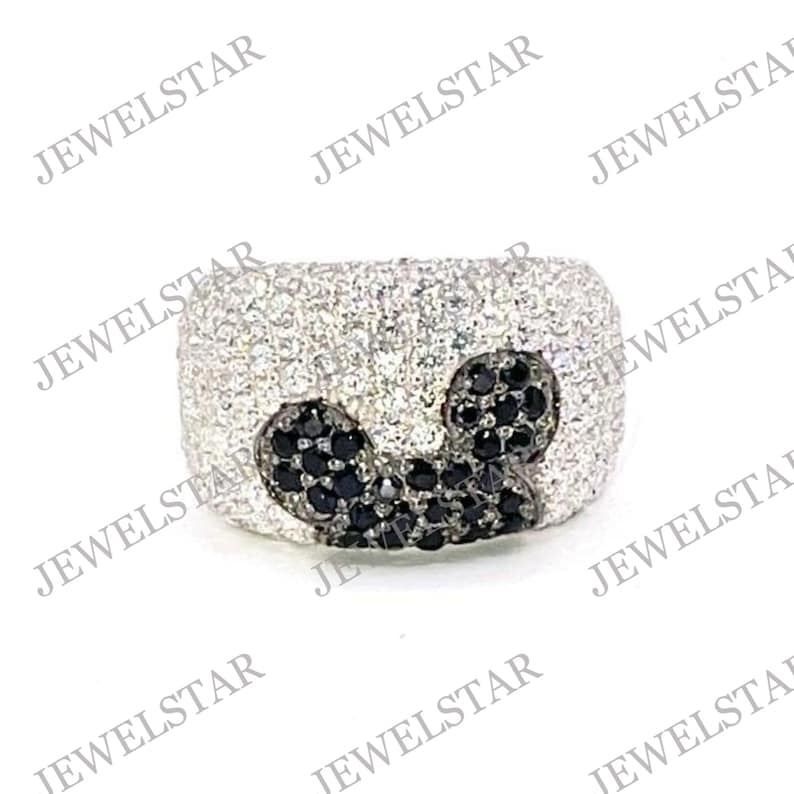 May include: A silver ring with a black and white Mickey Mouse design. The ring is covered in small, sparkling stones.