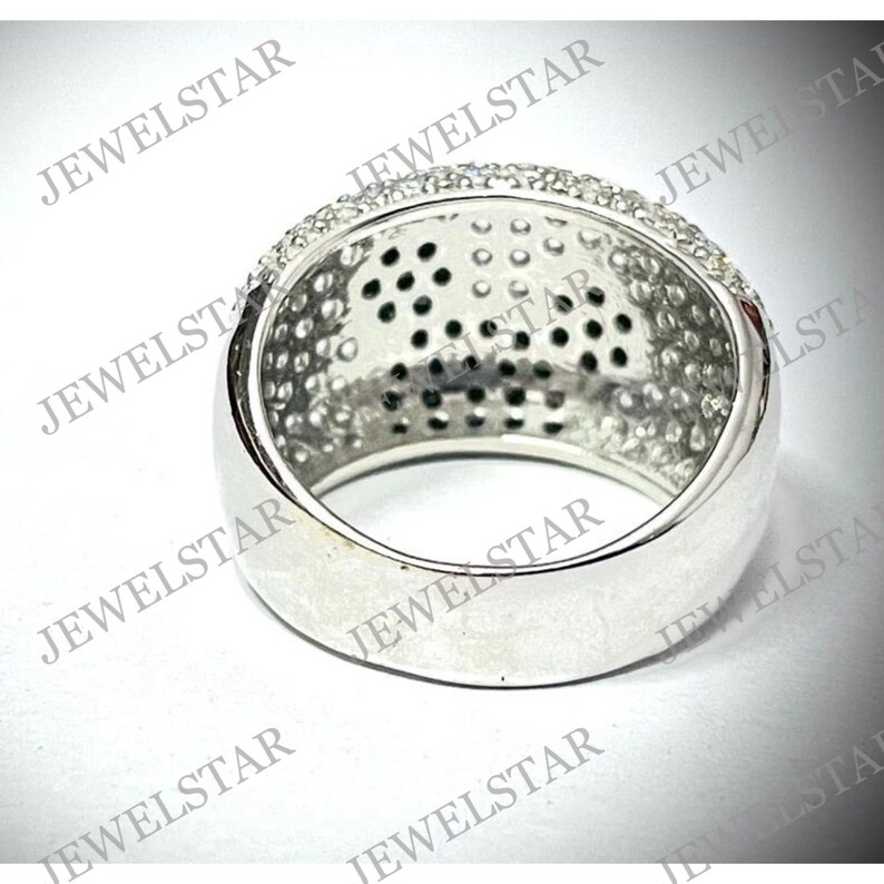 May include: A silver ring with a wide band and a row of small, clear stones around the top. The inside of the ring is smooth and polished.