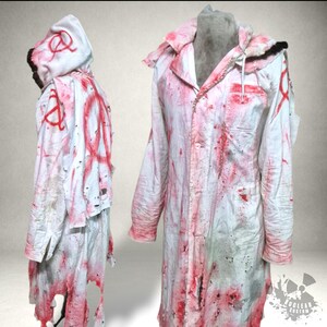 Może przedstawiać: Biały kostium z kapturem z czerwonymi plamami i oznaczeniami. Kostium ma zniszczony wygląd z rozdarciami i dziurami. Projekt obejmuje koszulę zapinaną na guziki i kaptur ze sznurkiem. Motyw horroru lub Halloween.