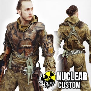 May include: A person wearing a brown and green, heavily distressed, leather and fabric costume with a large, metal chest piece. The costume is decorated with straps, buckles, and a large, metal arm piece. The person is holding a rifle in their right hand. The background is a white wall with the text "NUCLEAR CUSTOM" in black and yellow.