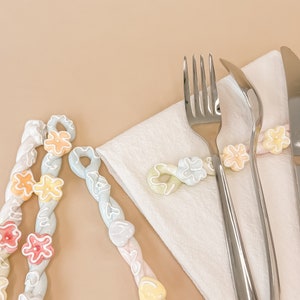 May include: Three pastel-colored, twisted, ceramic sticks with white flower designs. The sticks are arranged on a white napkin with two silver forks and a silver knife.