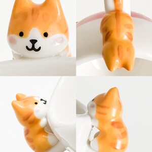 May include: A white ceramic mug with a cute orange and white cat figurine attached to the handle. The cat is in a sitting position with its tail wrapped around the handle.