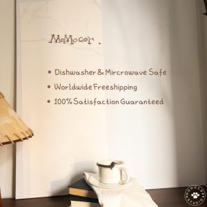 May include: A white ceramic mug with a dachshund dog design, resting on a saucer and a white cloth. The image also shows the text "MoMocor" and the words "Dishwasher & Microwave Safe".